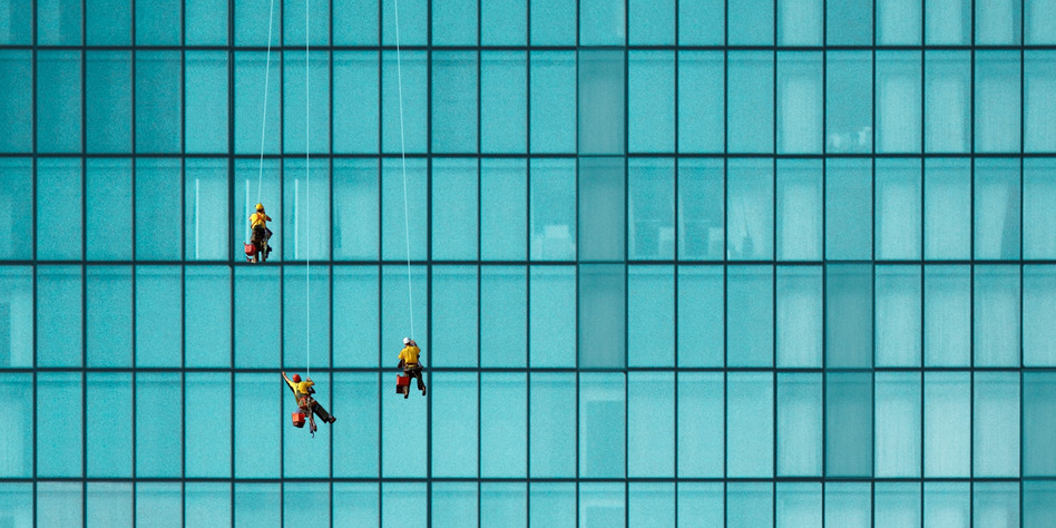 People cleaning a skyscraper's windows hanging from ropes